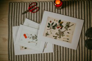 best print on demand products to sell in 2026 Top view of colorful pictures of different plants in frame placed on stripe carpet with candle and scissors on floor